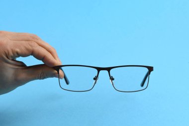 El ele tutuşan siyah gözlükler, mavi arka planda izole. Yüksek çözünürlüklü. Tam alan derinliği.