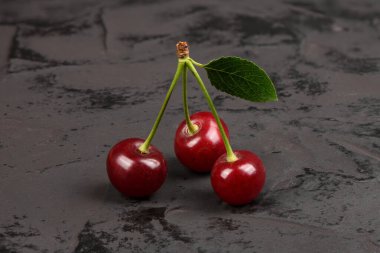 Siyah arka planda yeşil yapraklı taze kırmızı kirazlar. Doğal arka plan. Metin için boş alan.