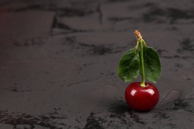 Siyah arka planda yeşil yapraklı taze kırmızı kirazlar. Doğal arka plan. Metin için boş alan.