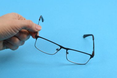 El ele tutuşan siyah gözlükler, mavi arka planda izole. Yüksek çözünürlüklü. Tam alan derinliği.