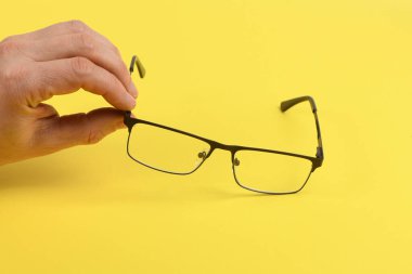 El ele tutuşan siyah gözlükler, sarı arka planda izole. Yüksek çözünürlüklü. Tam alan derinliği.