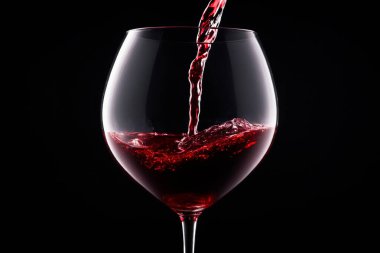 Kırmızı şarap bardağa doldurulur. Siyah arka planda bir kadeh kırmızı şarap..