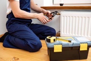 Isıtma radyatörünü tamir et. Adam ingiliz anahtarıyla radyatör onarıyor. Radyatörden hava çekiliyor.