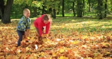 Erkek ve kız kardeşler sonbahar parkında akçaağaç yapraklarıyla oynuyorlar. Yüksek kalite 4k görüntü
