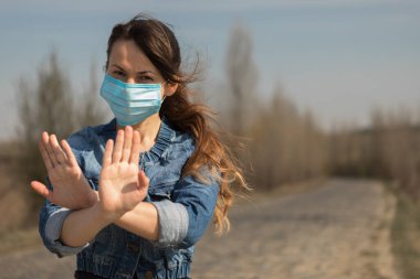 Koruyucu steril tıbbi maske takmış bir kadın dışarıda kameraya bakıyor. El Durdurma İşareti. Pandemik koronavirüs konsepti.
