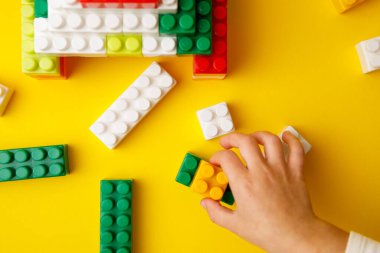 Elim renkli plastik bloğu istifliyor. Çocuk inşaatçıyla oynuyor.