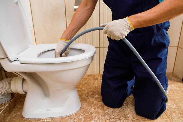plumber unclogging blocked toilet with hydro jetting at home bathroom. sewer cleaning service
