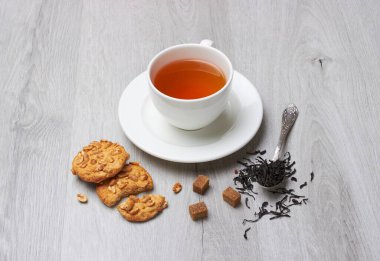 Bir fincan çay ve kurabiye, kaşık, şeker, hafif ahşap bir arka planda
