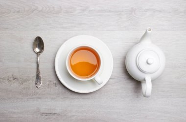 Bir fincan çay ve çaydanlık, kaşık, hafif ahşap arka planda.