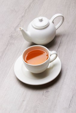 Bir fincan çay ve çaydanlık, hafif ahşap bir arka planda.