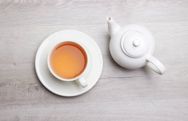 Bir fincan çay ve çaydanlık, hafif ahşap bir arka planda.