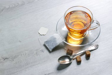 Bir fincan çay ve çay poşeti, kaşık, şeker, hafif ahşap arka planda.