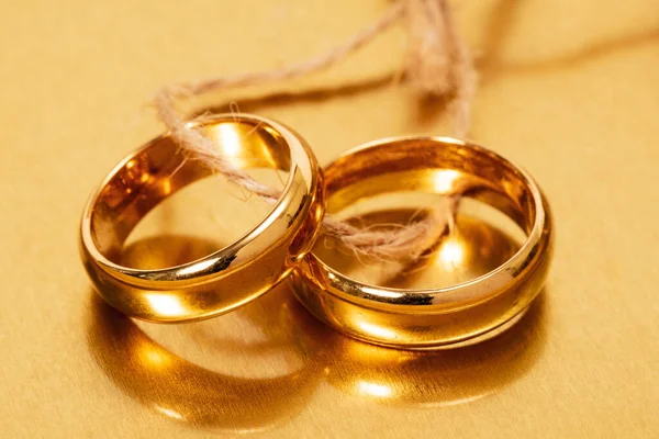 Two gold wedding rings tied with string on the golden background. Close-up view.