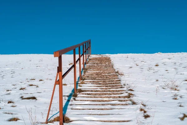 Stairs stretching up to a hill with a melting snow.The concept of career growth or the road to heaven. Steps on a high hill lead to the sky.