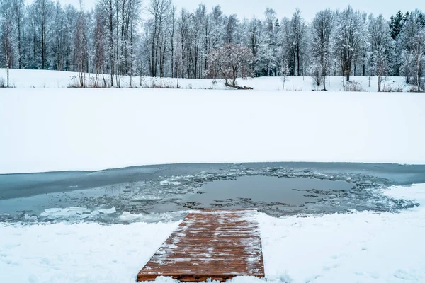 An ice hole on a frozen lake with a snow-covered wooden path descending into the water.Care about body health in winter time.