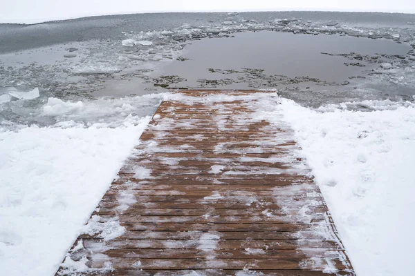 Ice swimming place with a snow-covered wooden path descending into the water.Care about body health in winter time.