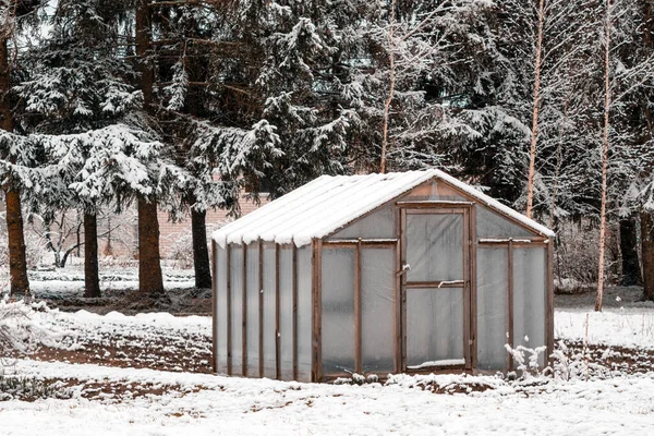 Wooden diy homemade greenhouse covered with polythene and snow in winter.