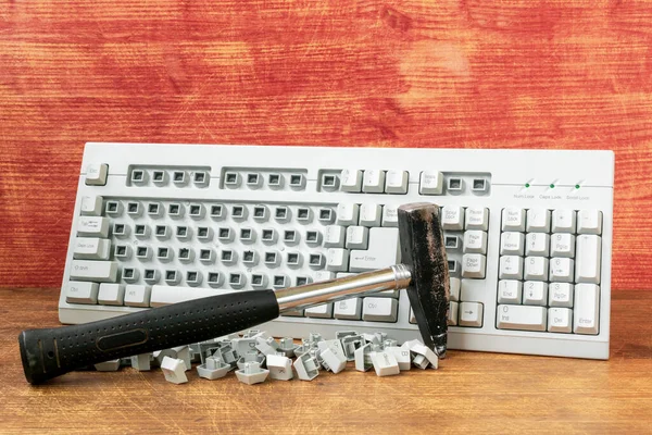 Broken computer keyboard and hammer on wooden background. Hammer and computer keyboard with damaged keys.