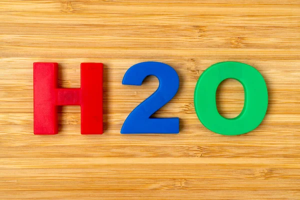 stock image The lettering of H2O on brown wood  background. Formula H2O on wooden background.