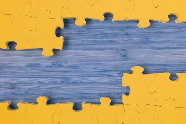 The frame from yellow puzzle on blue wooden background. Copy space.