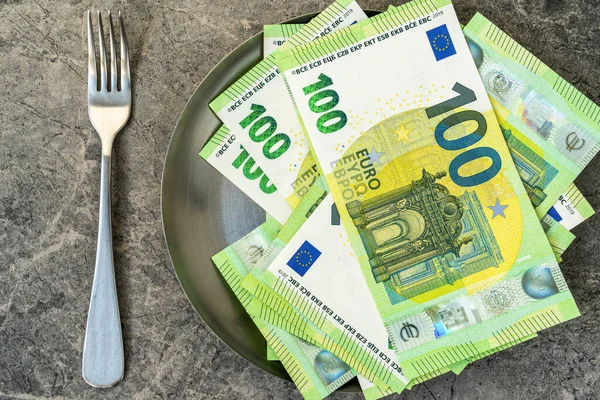 ユーロ紙幣は テーブルの上にフォークでプレートに横たわっています 紙幣を食べる象徴的なイメージ インフレの影響で食料価格が上昇しています — ストック写真
