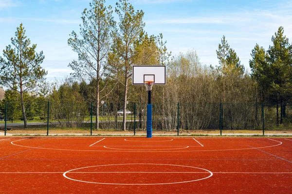 Empty basketball court on sunny day. Basketball hoop and court with nature background.