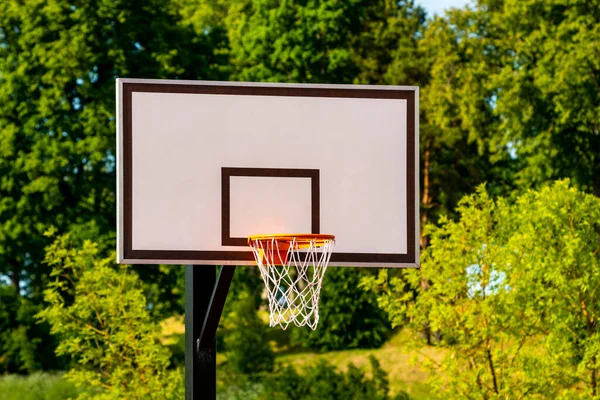 Basketball basket in an outdoor court with a green trees on background