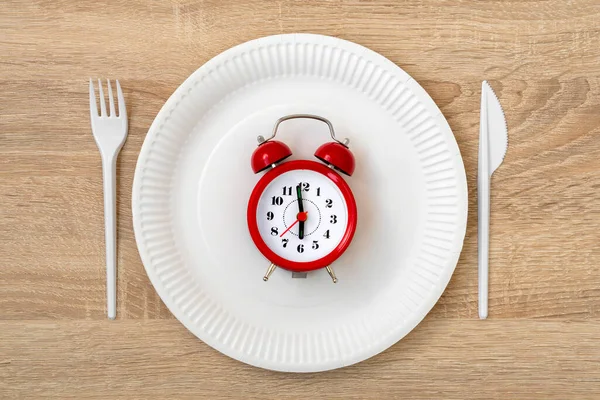赤い目覚まし時計 使い捨てプレート フォーク ナイフで朝食時間の概念 健康的な食事の概念 夕方６時以降は食べてはいけない — ストック写真