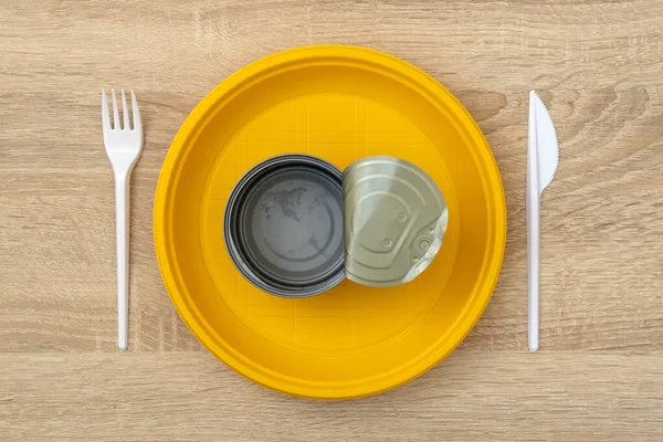 A disposable plate plate with an opened empty tin can surrounded by fork, and knife cutlery. Scarcity of food and world hunger and inequality concept. Top view.