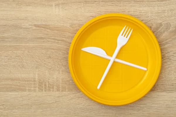 木製のテーブルの上にフォークとナイフで使い捨てのプラスチックプレート トップビュー コピースペース — ストック写真