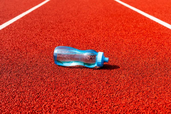 A water bottle on a running track outside.The Importance of Water While Exercising. Drink more water.