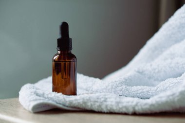 Kehribar cam serumu, yağ damlası şişesi masa maketinde beyaz havlu, kozmetik konteynır çekimleri, bakım ürünü şablonu