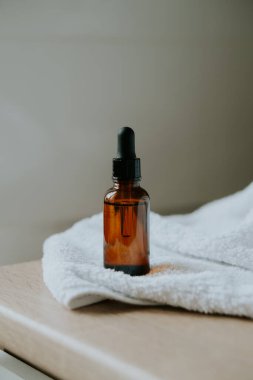 Kehribar cam serumu, yağ damlası şişesi masa maketinde beyaz havlu, kozmetik konteynır çekimleri, bakım ürünü şablonu