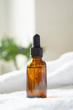 Kahverengi kehribar rengi serum serumu yağ düşürücü şişesi ve beyaz havlu. Masa maketi, kozmetik konteynır gerçek iç mekan, bakım ürünü şablonu.