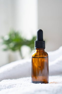 Kahverengi kehribar rengi serum serumu yağ düşürücü şişesi ve beyaz havlu. Masa maketi, kozmetik konteynır gerçek iç mekan, bakım ürünü şablonu.