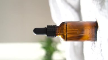 Kahverengi kehribar rengi serum serumu, yağ damlası şişesi ve beyaz havlu. Masa modeli, gerçek iç mekan kozmetik konteynırın dikey görüntüsü, bakım ürünü şablonu.