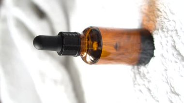 Kahverengi kehribar rengi serum serumu, yağ damlası şişesi ve beyaz havlu. Masa modeli, gerçek iç mekan kozmetik konteynırın dikey görüntüsü, bakım ürünü şablonu.