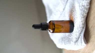 Kehribar cam serumu, yağ damlası şişesi ve beyaz havlu. Masa maketi, kozmetik kap dikey çekim, bakım ürünü şablonu.