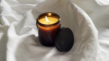 Kehribar cam kavanozda yanan mum beyaz kumaş üzerinde kokulu mum keten arka planda yakın plan çekimi