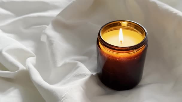 Brennende Kerze Bernsteinglas Auf Weißem Tuch Duftkerze Auf Leinenhintergrund Nahaufnahme — Stockvideo