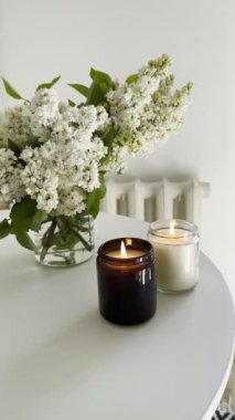 Yuvarlak beyaz masa üzerinde yanan iki mum ve bir demet leylak. Gerçek ev minimalist İskandinav iç mekan üst görünümü.