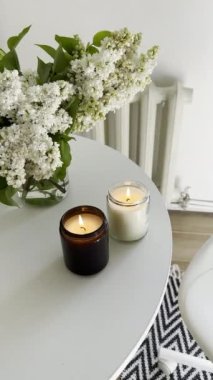 Yuvarlak beyaz masa üzerinde yanan iki mum ve bir demet leylak. Gerçek ev minimalist İskandinav iç mekan üst görünümü.