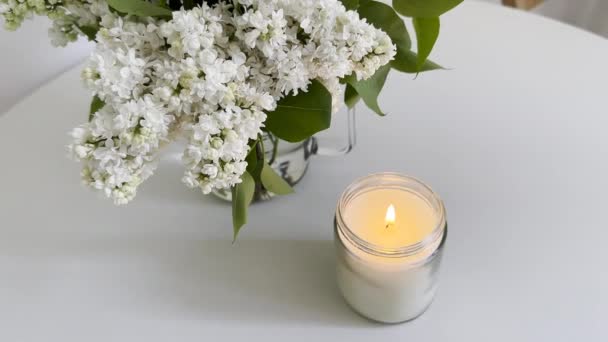 Brennende Kerze Klarem Glas Und Weißem Fliederstrauß Auf Weißem Tisch — Stockvideo