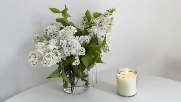 Brennende Kerze Klarglasgefäß Und Weißer Fliederstrauß Auf Weißem Tisch Kerzenvideo — Stockvideo