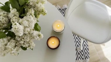 Yuvarlak beyaz masa üzerinde yanan iki mum ve bir demet leylak. Gerçek ev minimalist İskandinav iç mekan üst görünümü.