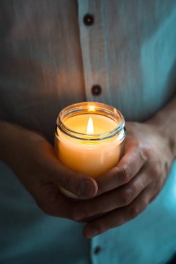 Elinde yanan bir mum tutan adam, mum kavanozlu zarif genç adam, yakın çekim, meditasyon ve farkındalık konsepti.