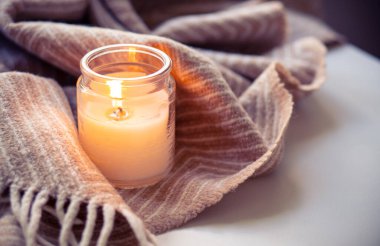 Bir mum ve yumuşak bir battaniye, sonbahar ve kışın rahatlamak ve rahatlamak için ideal sıcak, rahat bir atmosfer yaratır.