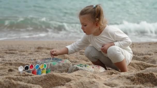 小さな女の子が砂浜で絵を描いている 休暇のために遊び — ストック動画