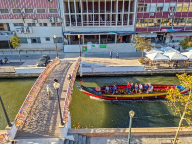 Aveiro, Portekiz - 27 Ağustos 2023: Geleneksel olarak kurdelelerle süslenmiş köprü ile kanala açılan tekne. Tekne turu şehrin en ünlü yeridir..