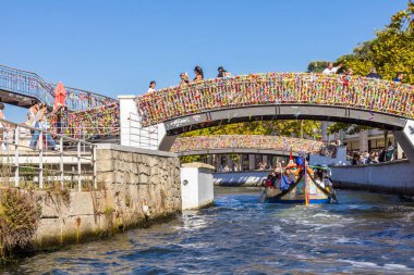Aveiro, Portekiz - 27 Ağustos 2023: Geleneksel olarak kurdelelerle süslenmiş köprü ile kanala açılan tekne. Tekne turu şehrin en ünlü yeridir..